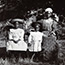 Semane Khama at right, seated, with two children, one of whom is standing, one of whom is seated.