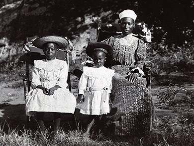 Semane Khama at right, seated, with two children, one of whom is standing, one of whom is seated.